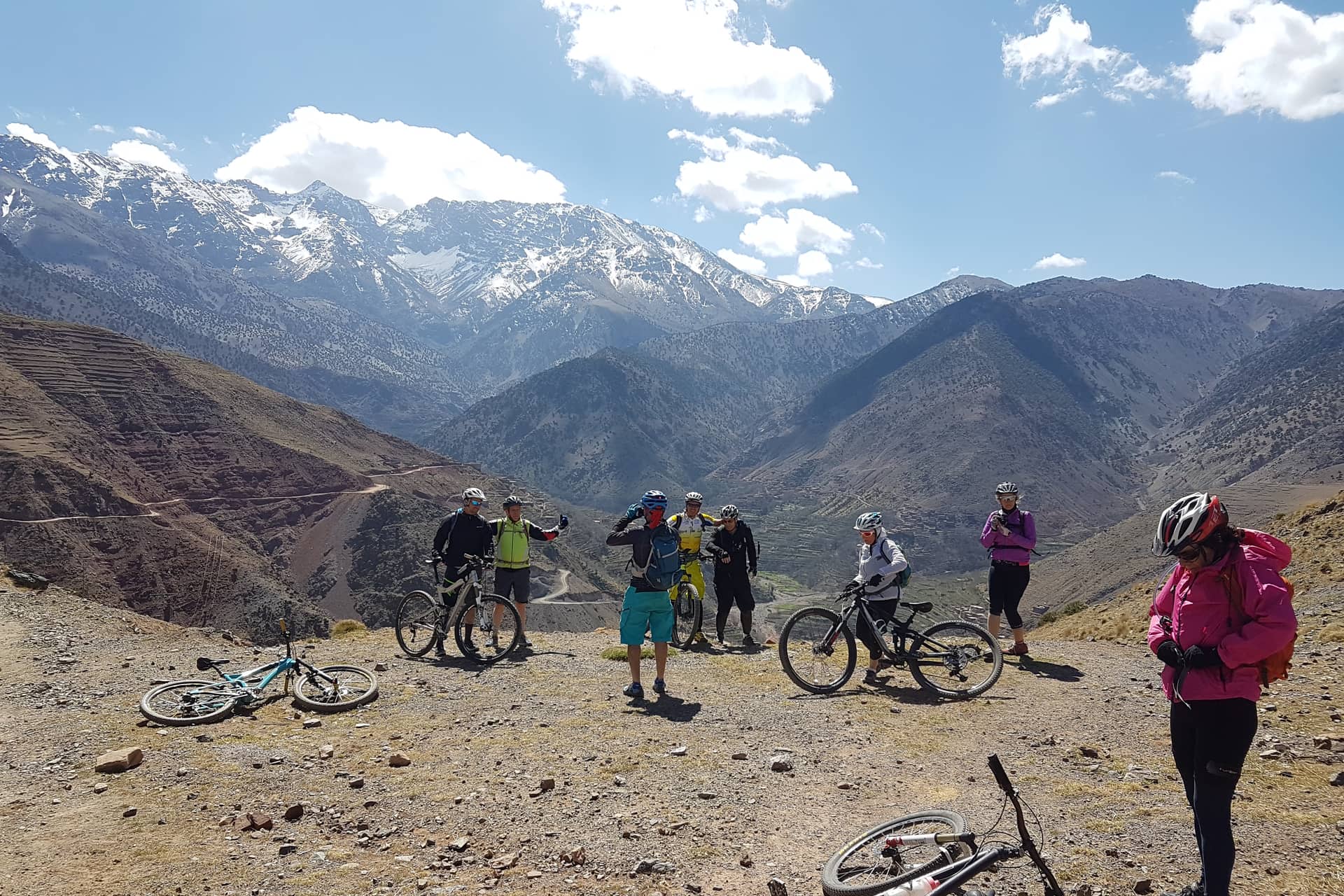 Group of riders stopped at a viewpoint with the snow-covered High Atlas behind them