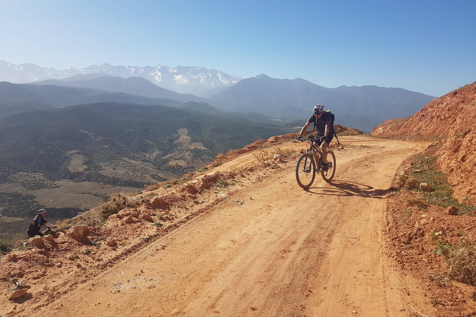 Mountain biker climbing a red earth piste towards the snow-capped Atlas range