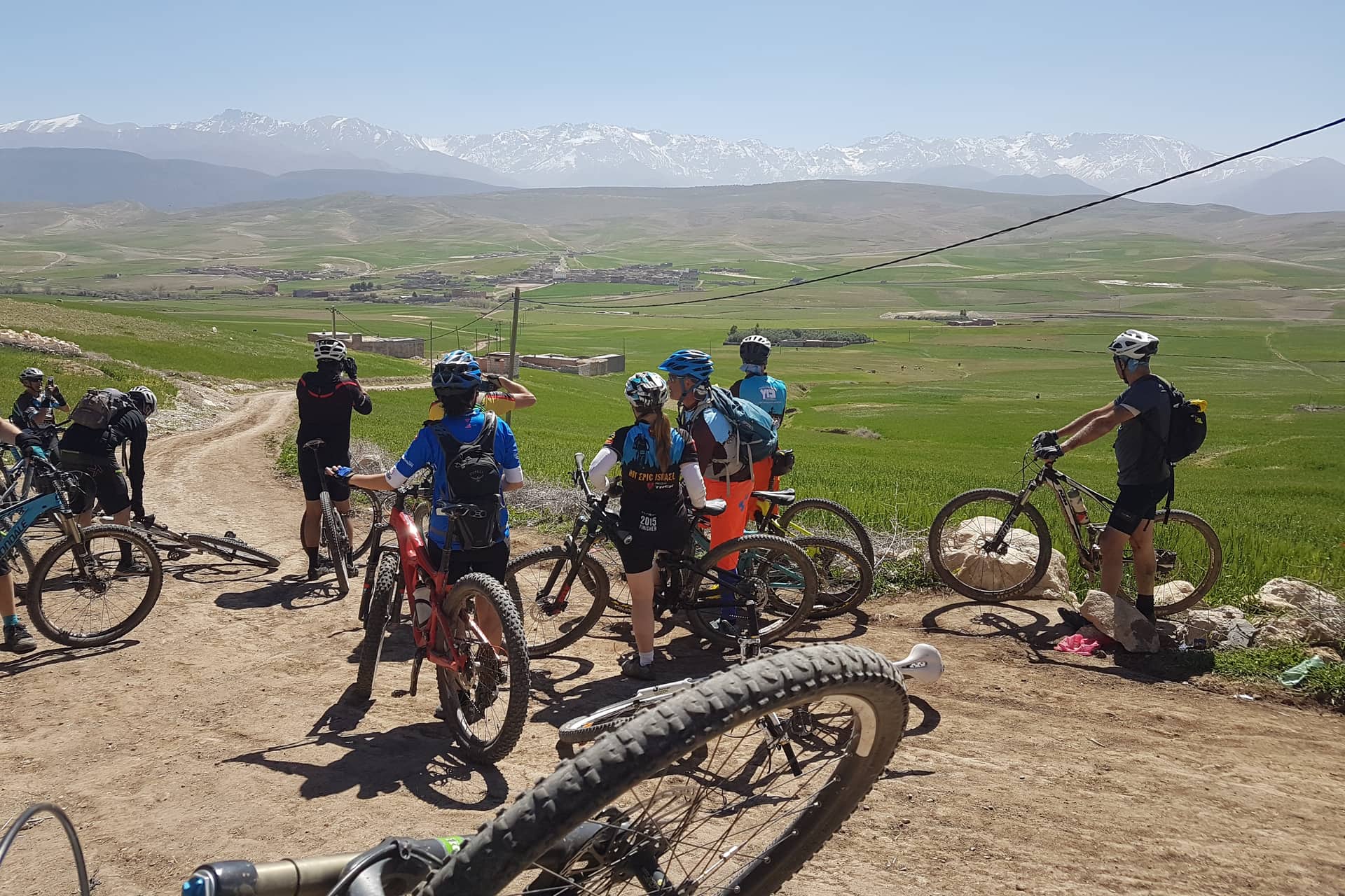 Riders regrouping on a piste above green plains with the High Atlas behind