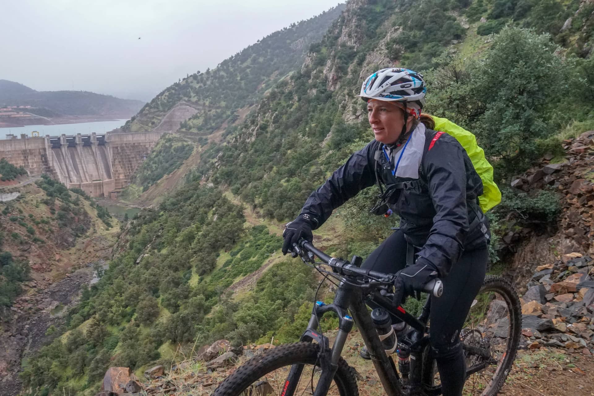 Rider on a wet hillside trail high above a reservoir and its dam wall