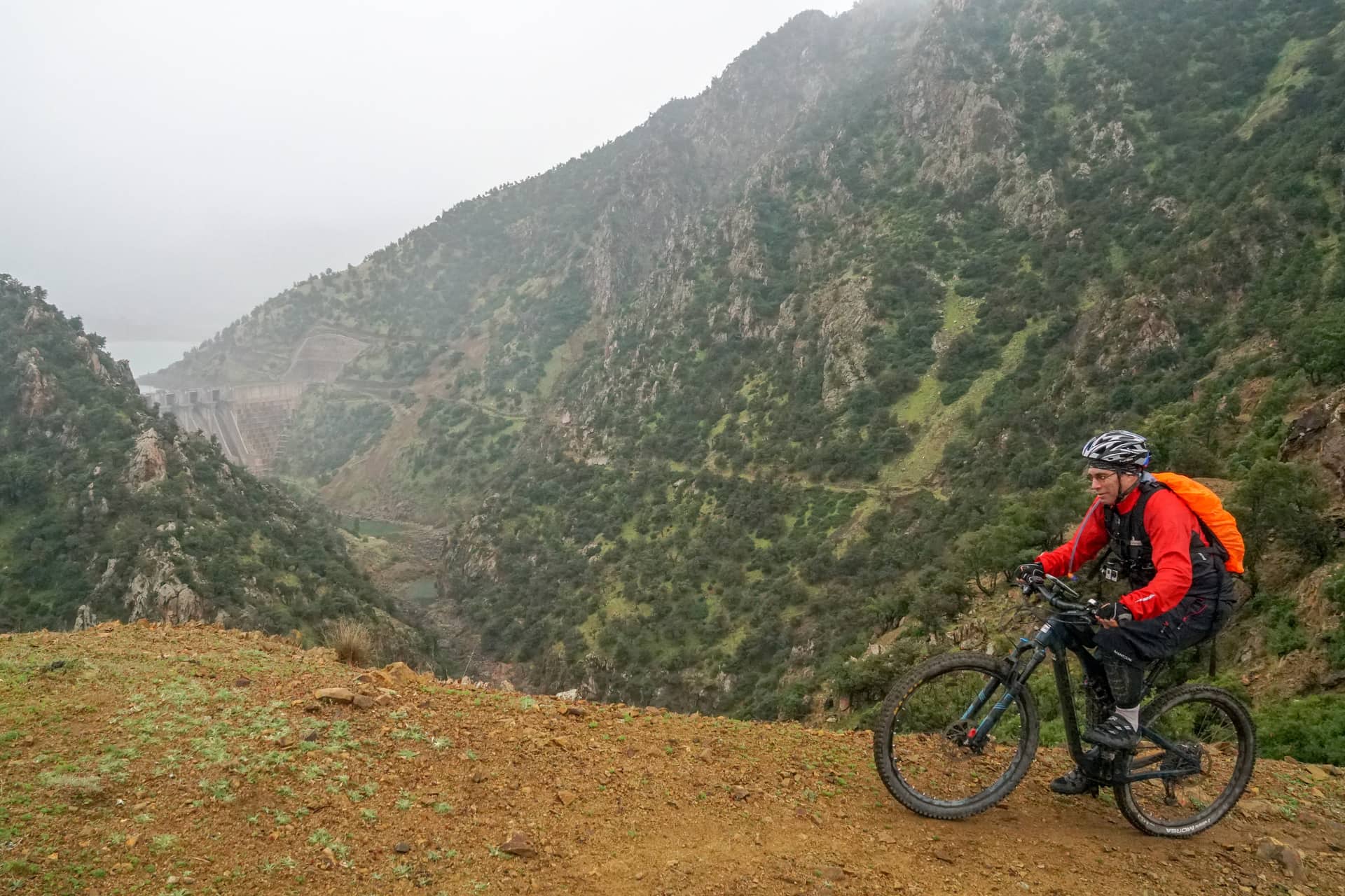 Rider pausing on a red-earth trail above a deep wooded valley in the High Atlas