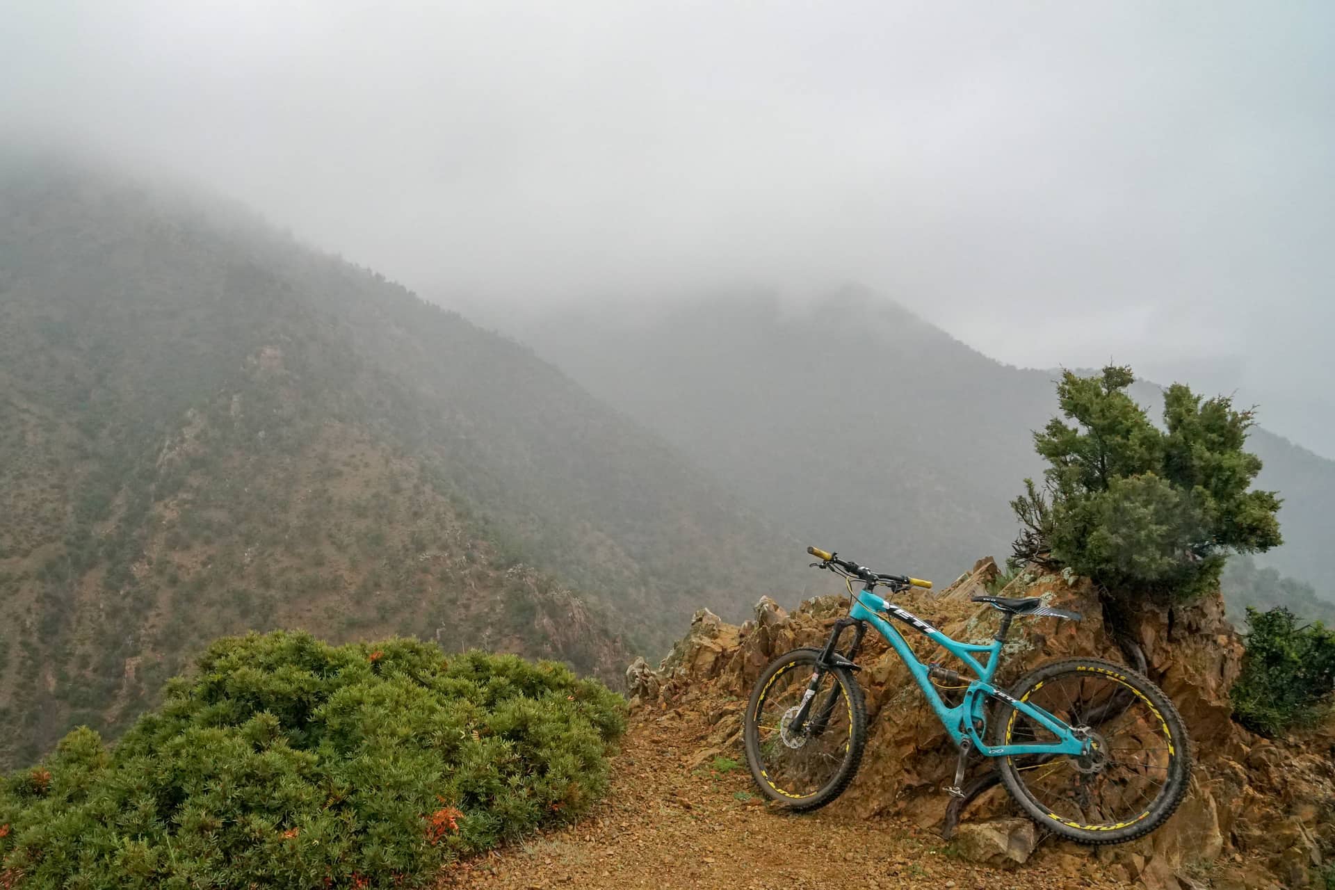 A mountain bike resting against rock at a misty pass in the Atlas
