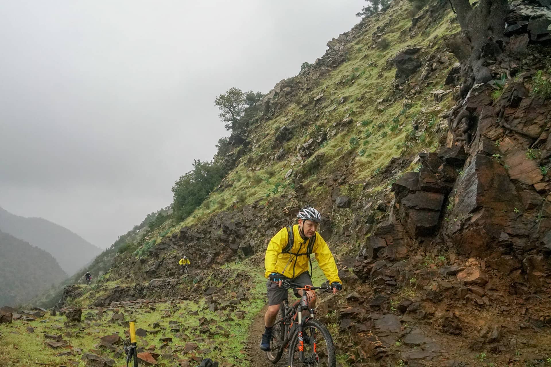 Riders strung out along a stony traverse below a misty ridge