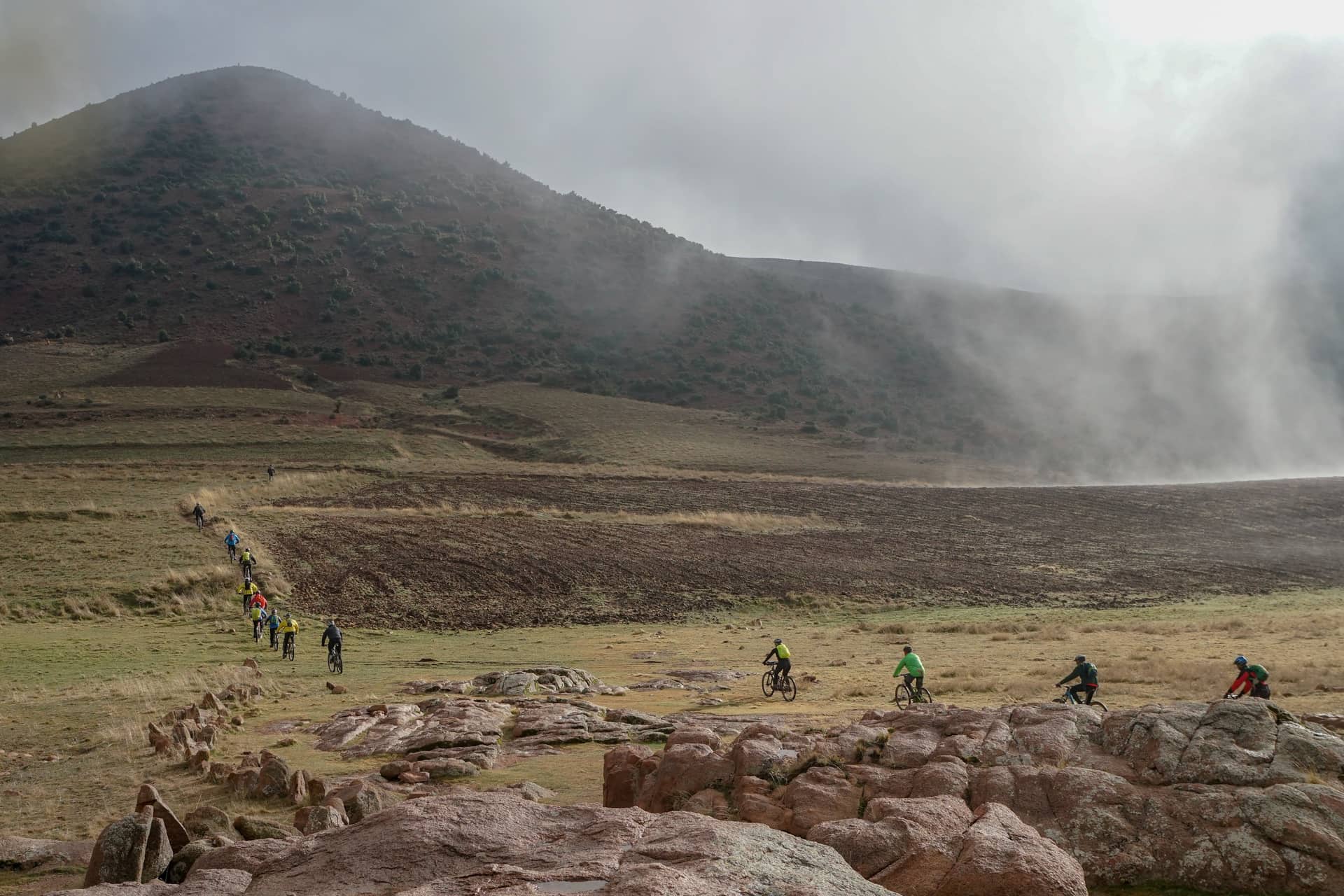 A line of riders crossing open upland pasture as mist rolls off the hill