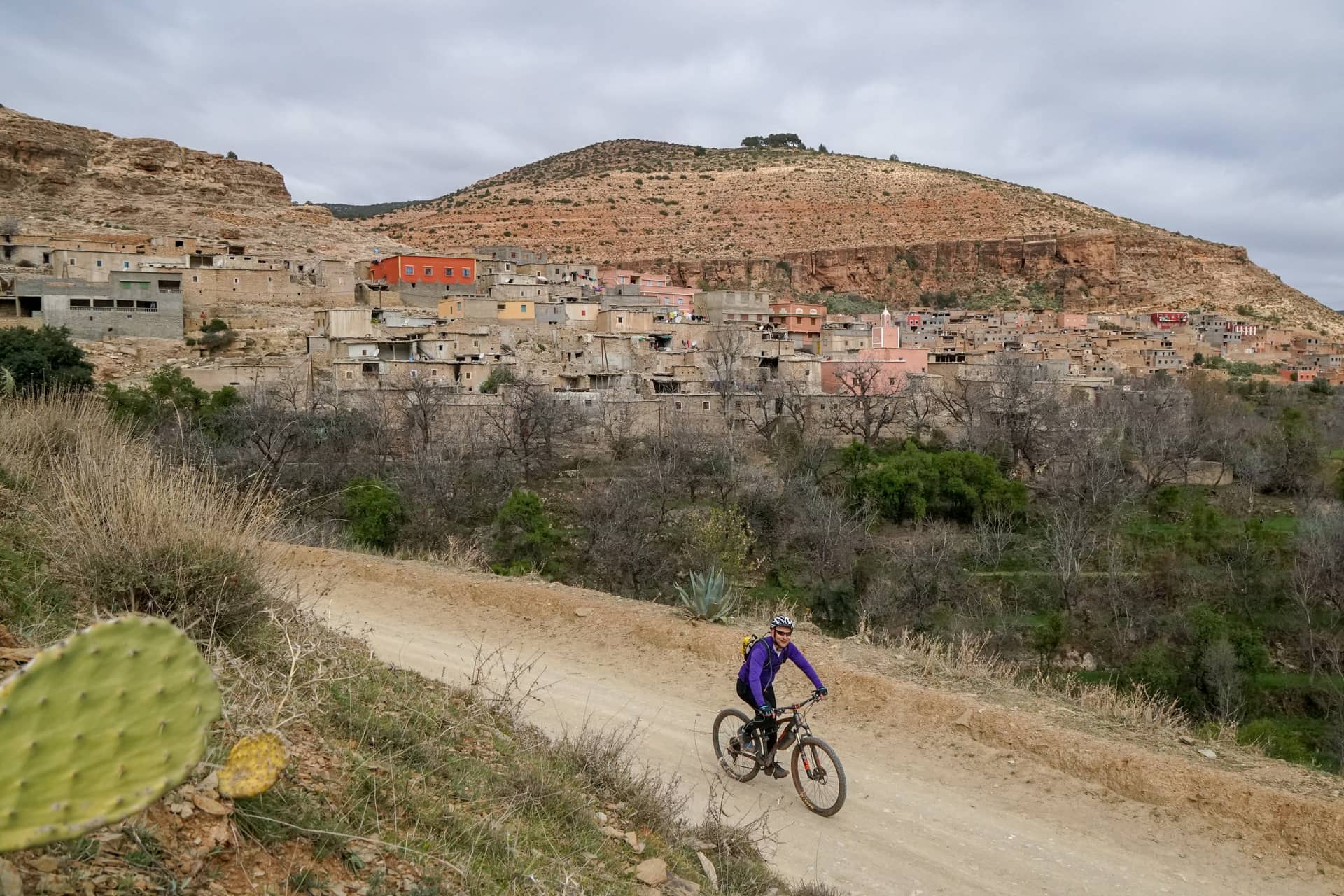 Rider on a wide dirt piste below an Amazigh village built into the hillside