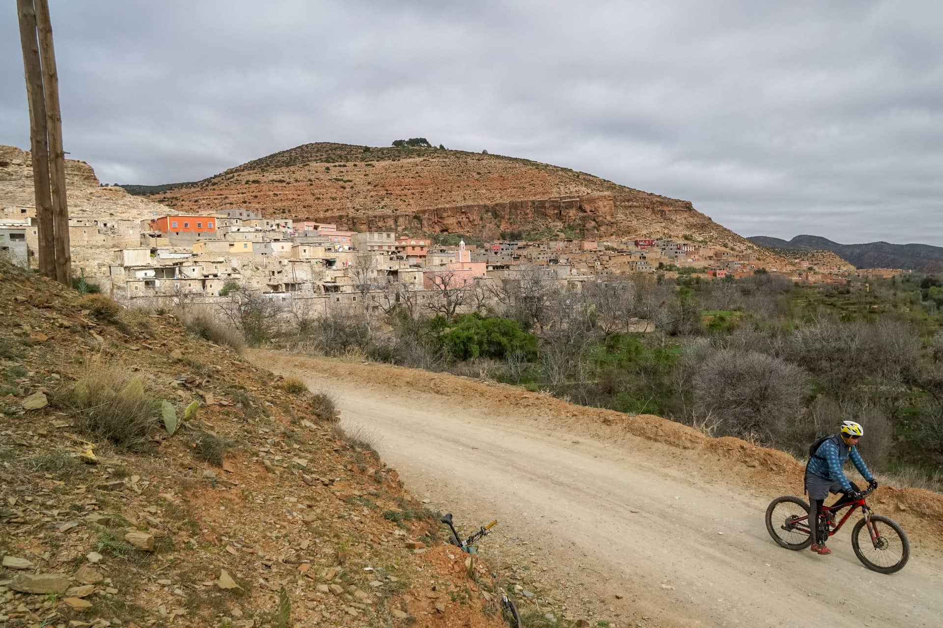 Rider on a dirt road below a hillside village of stacked earth houses