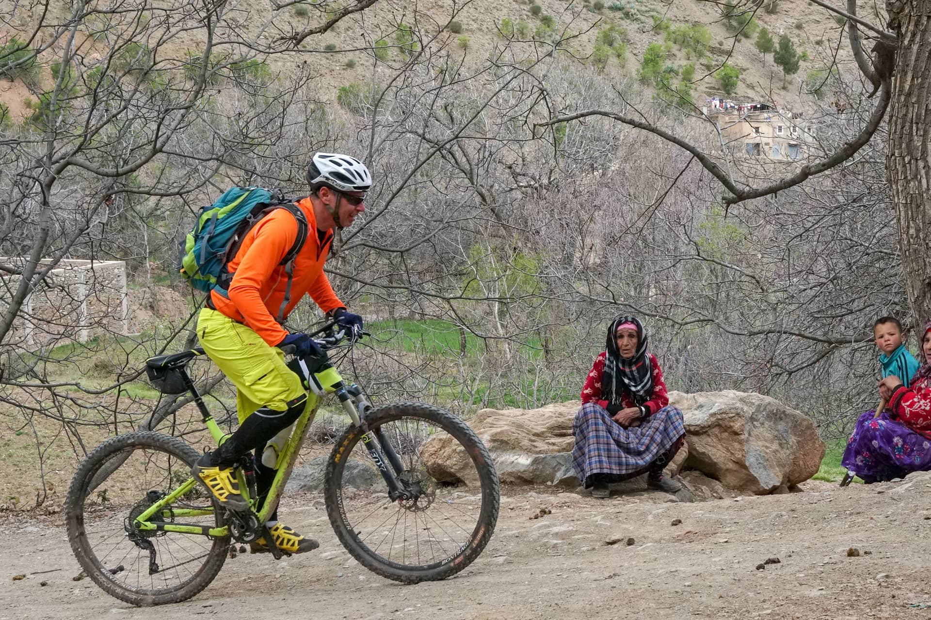 A rider passing an Amazigh family sitting by the trail in an Atlas village