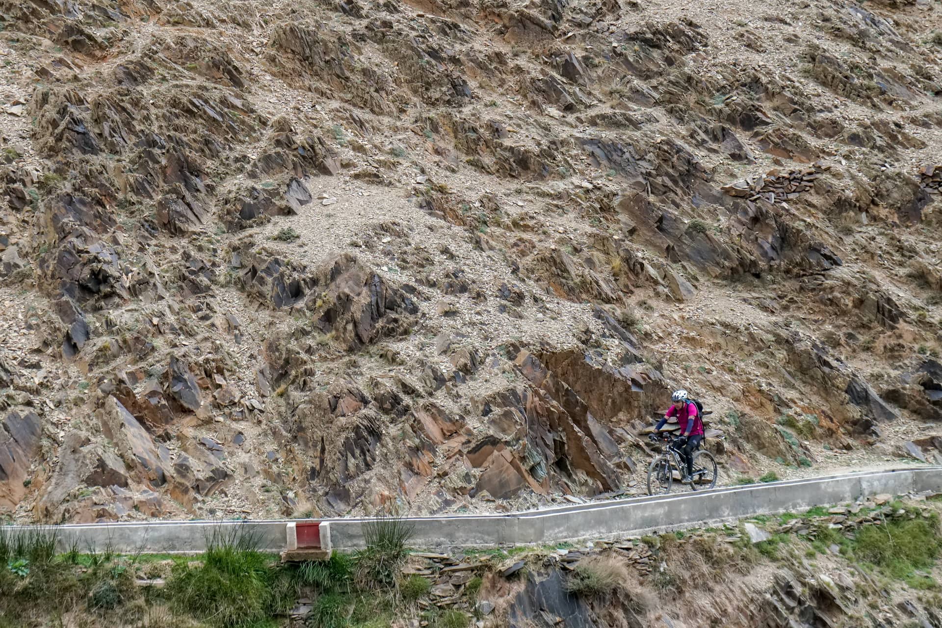 Lone rider on a narrow mountain road cut into a vast shattered rock face