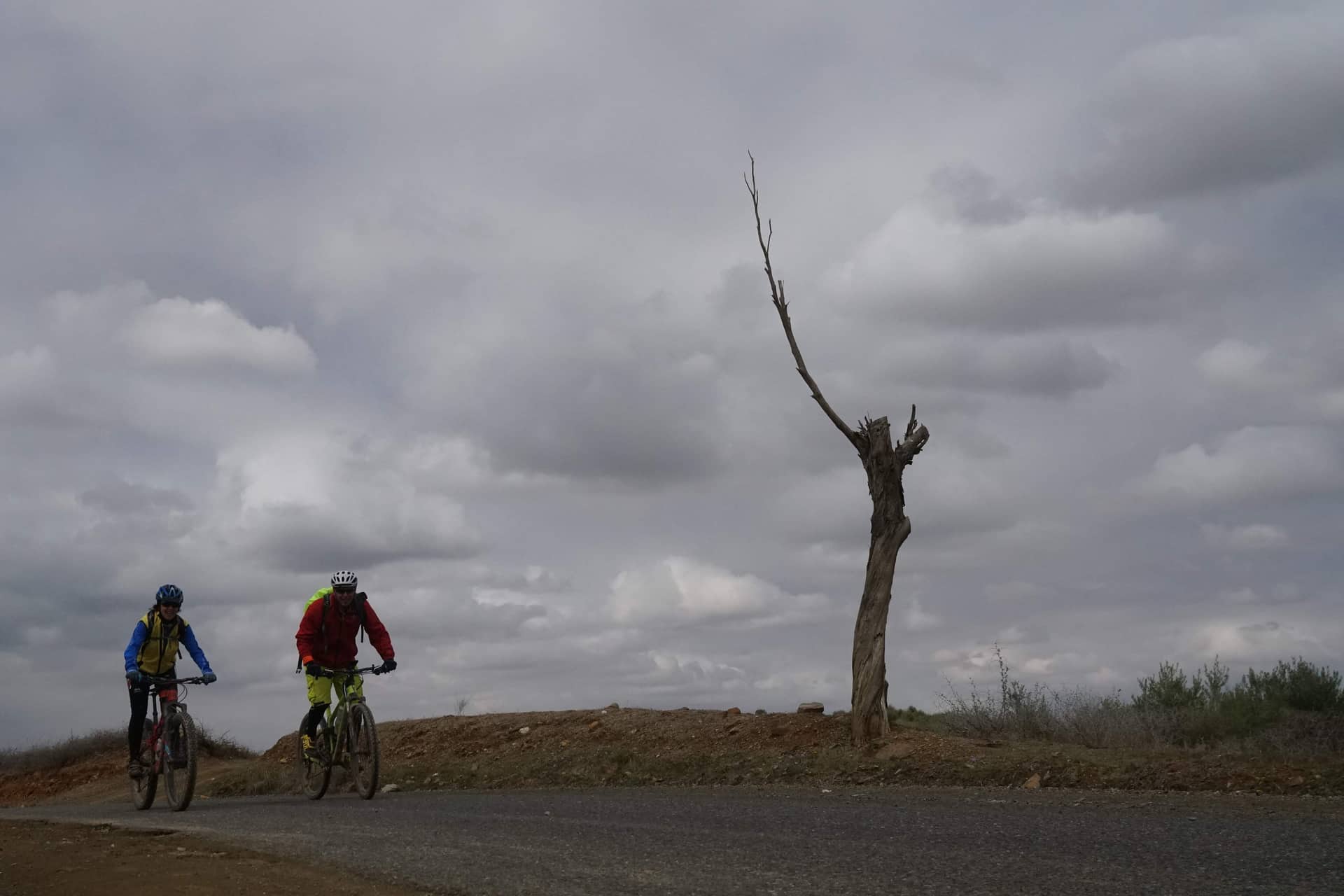 Two riders on open, flat desert ground under a wide cloudy sky