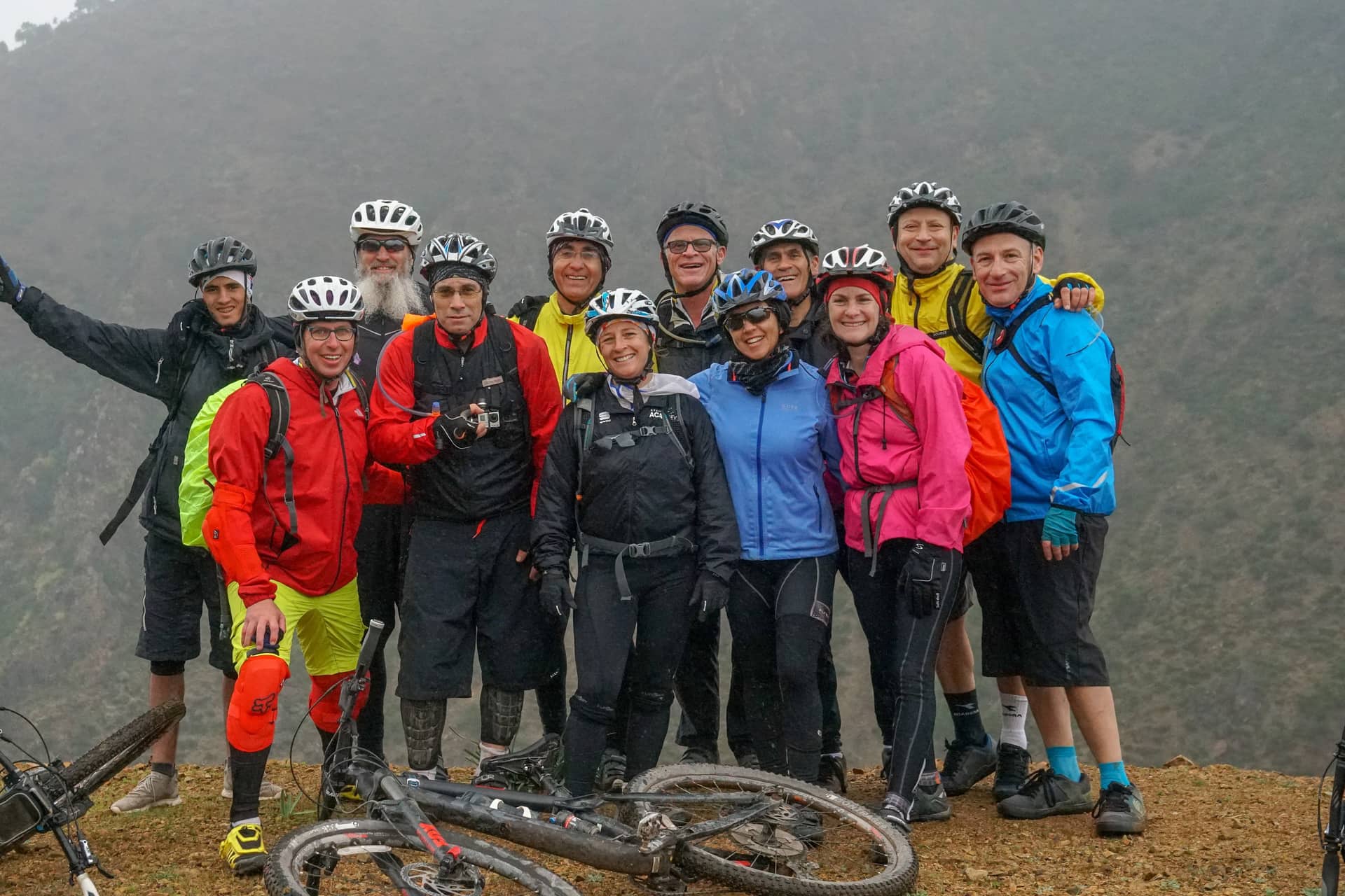 A full group of riders together at a misty summit, bikes laid down