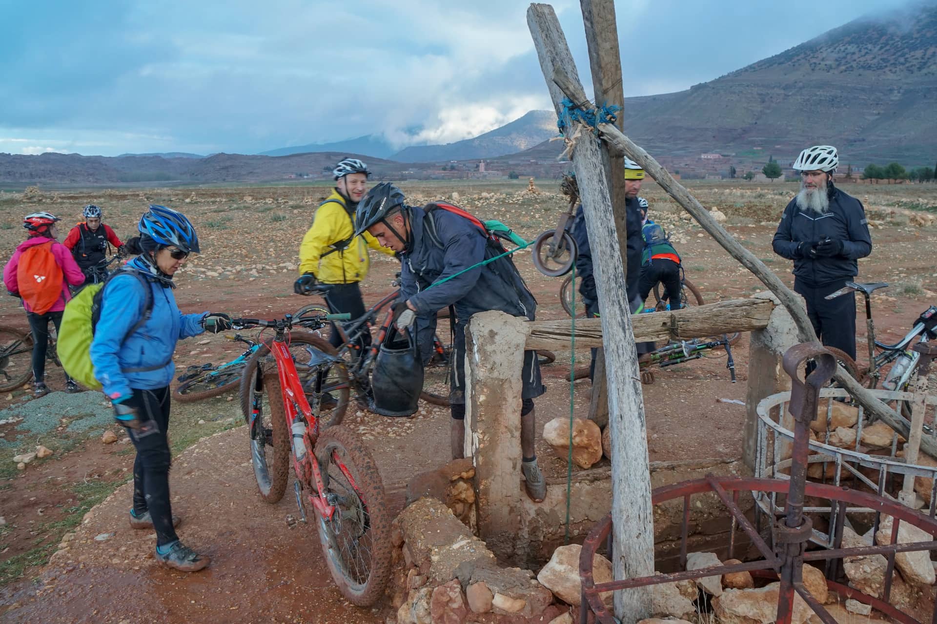 Riders and guides drawing water from a village well, with the Atlas behind